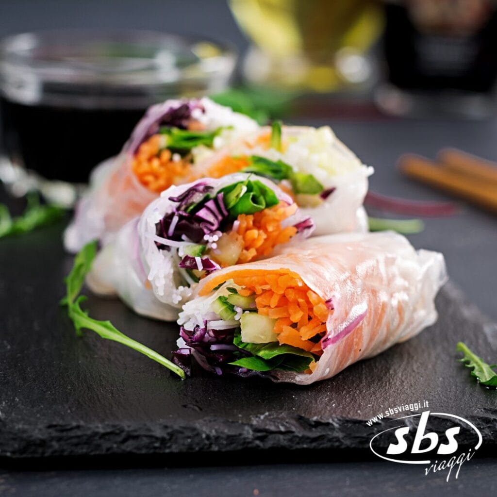 Due involtini primavera freschi, ispirati ai viaggi in Vietnam, sono farciti con carote tritate, cavolo, verdure e spaghetti di riso su un piatto di ardesia, serviti con una salsa piccante sullo sfondo.
