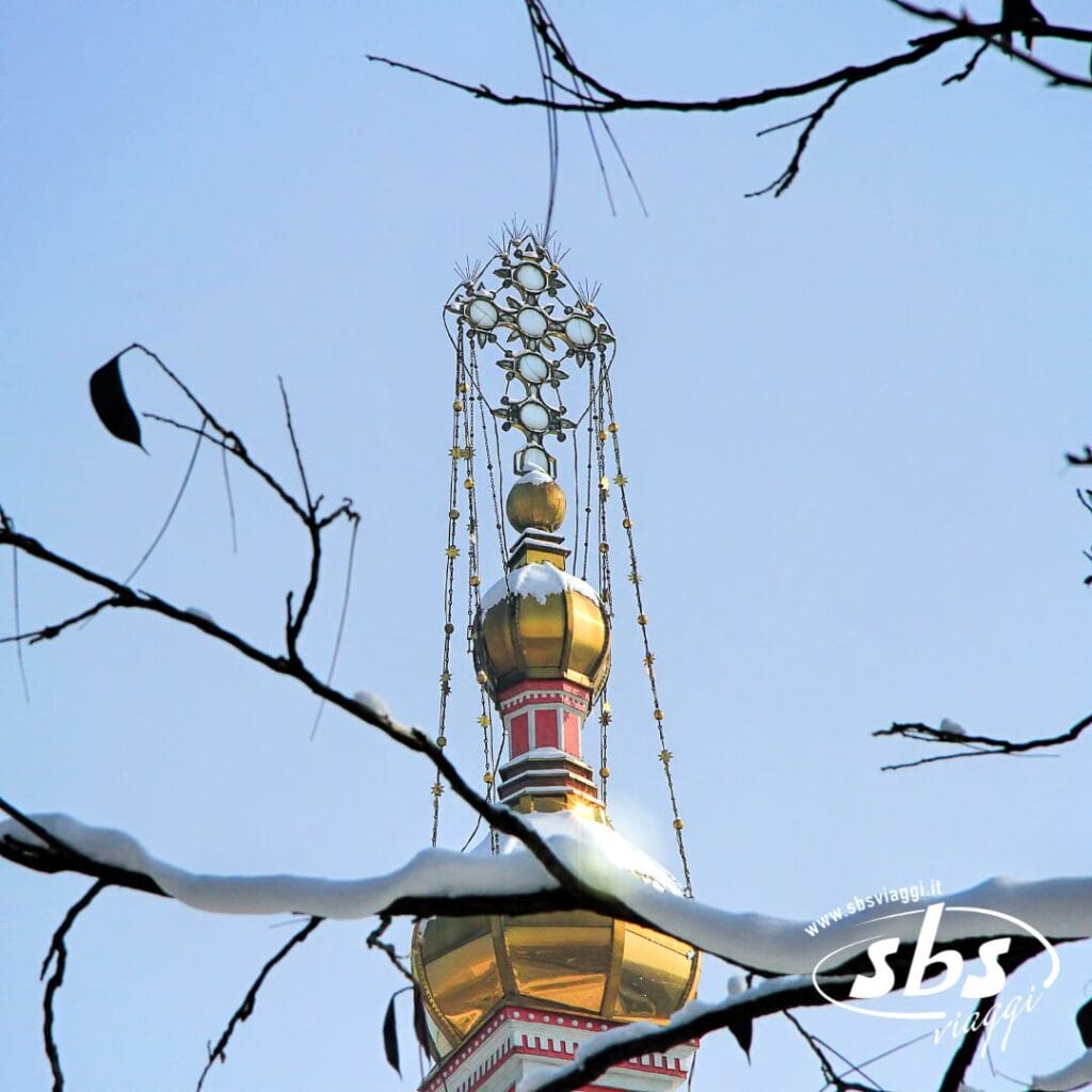 La cupola dorata a cipolla di una chiesa ortodossa russa con una croce decorativa, incorniciata da rami di alberi innevati e contro un cielo azzurro terso: uno scenario pittoresco da scoprire durante il tour del Kazakistan.