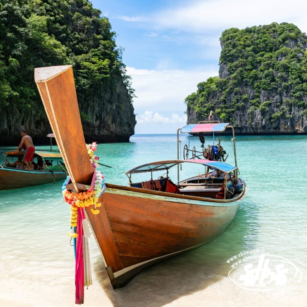 Una barca a coda lunga in legno su acque turchesi e cristalline, con scogliere e vegetazione lussureggiante sullo sfondo: uno scenario iconico di Phuket, perfetto per la tua avventura Estensione Mare Phuket o Tour Thailandia.