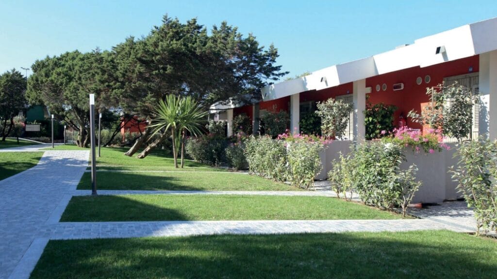 Moderno edificio a un piano con pareti rosse, un rigoglioso prato verde, arbusti e un sentiero pavimentato: uno spazio invitante realizzato con elementi di design ispirati alla Bozza automatica.