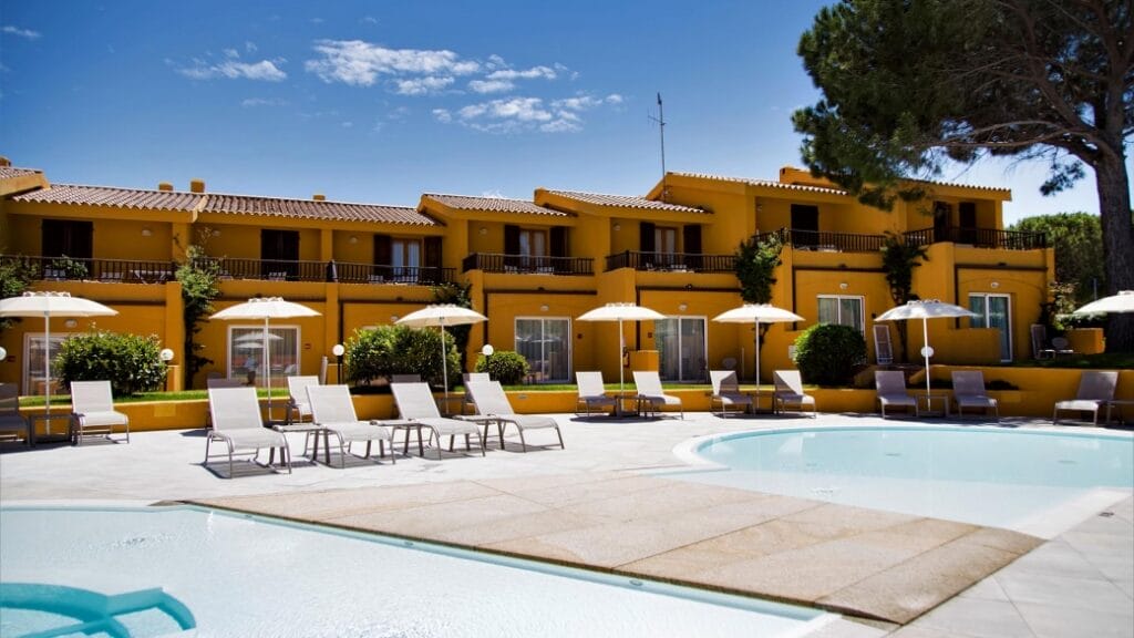 Lettini e ombrelloni accanto a una piscina con un edificio giallo dell'hotel e un cielo azzurro e limpido sullo sfondo creano la perfetta atmosfera Bozza automatica per una vacanza all'insegna del relax.