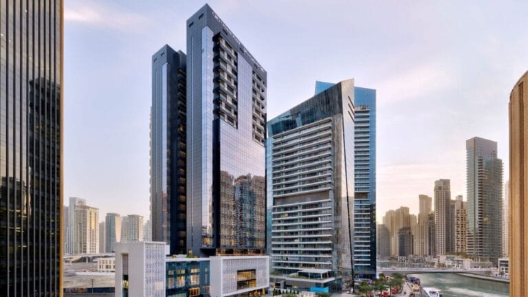 Alti grattacieli moderni con facciate in vetro nello skyline di una città al tramonto, con altri edifici sullo sfondo.