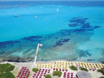 Vista aerea di una spiaggia con ombrelloni colorati, acqua azzurra e cristallina e diverse barche che galleggiano al largo, immortalata in una splendida bozza automatica.