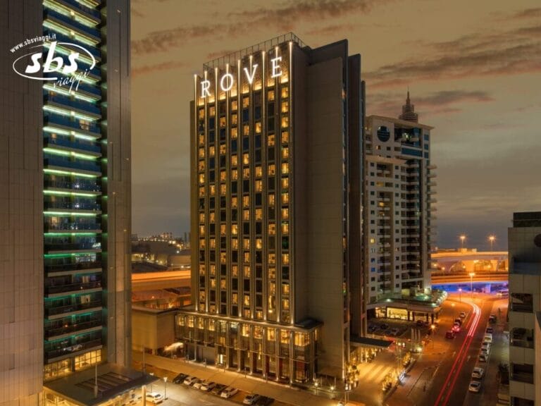 Vista notturna dell'edificio illuminato dell'hotel Rove, una presenza sorprendente tra le luci della città e gli alti edifici vicini, catturata nei minimi dettagli con Bozza automatica.