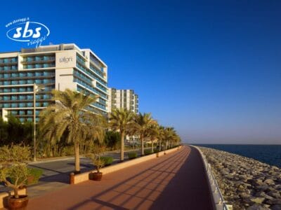 Un moderno hotel e palme costeggiano un soleggiato lungomare, caratterizzato da una costa rocciosa sotto un cielo azzurro e terso: un luogo invitante, perfetto per preparare la tua prossima Bozza automatica.