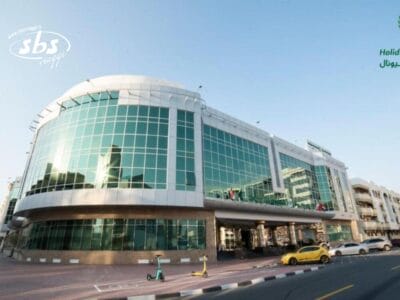 Moderno edificio con facciata in vetro su una strada cittadina, con auto, scooter elettrici e una Bozza automatica parcheggiati all'esterno.