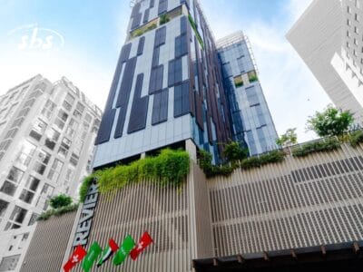 Moderno edificio alto con Bozza automatica, caratterizzato da vegetazione e bandiere sulla facciata, visto da un'angolazione bassa contro il cielo.