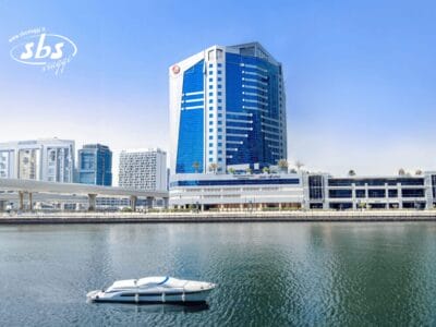 Un moderno edificio alberghiero in vetro blu in riva all'acqua con una piccola barca bianca che galleggia in primo piano.