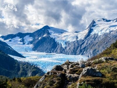 Montagne innevate con un ghiacciaio che scorre tra le cime, sfondo roccioso e cielo parzialmente nuvoloso.