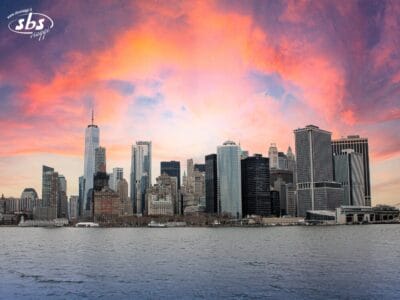 Vivi un Tour New York esclusivo: ammira lo skyline di Manhattan dall'acqua al tramonto, con gli alti edifici che si stagliano contro un suggestivo cielo rosa e arancione.