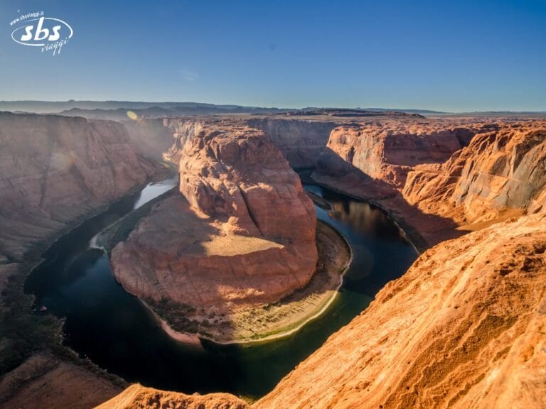 Vista aerea di Horseshoe Bend, una delle attrazioni principali del Tour del Golden West, dove il fiume Colorado si snoda attorno a una formazione di arenaria sotto un cielo azzurro e terso.