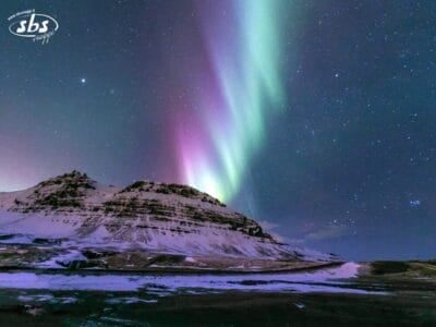 La Forza della Natura è in piena mostra quando l'aurora boreale, con le sue tonalità verdi e viola, splende sopra una montagna innevata sotto un cielo notturno stellato.