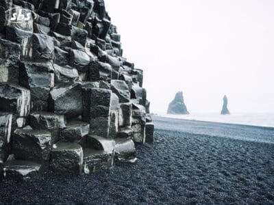 Colonne di basalto spigolose su una spiaggia di sabbia nera in Islanda, con faraglioni avvolti nella nebbiosa luce autunnale.