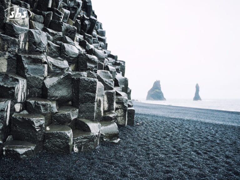 Colonne di basalto spigolose su una spiaggia di sabbia nera in Islanda, con faraglioni avvolti nella nebbiosa luce autunnale.