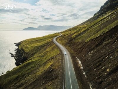 Una strada costiera tortuosa lungo la famosa Ring 1 dell'Islanda, delimitata da colline erbose e dal mare sotto un cielo parzialmente nuvoloso: perfetta per un'avventura Fly & Drive.