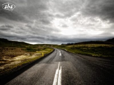 Una strada rurale tortuosa sullo Snaefellsnes si estende in lontananza sotto un cielo nuvoloso e coperto, con verdi colline su entrambi i lati: una scena classica del Ring 1 in Islanda.