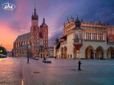 Rynek Główny, la piazza principale di Cracovia, in Polonia, con la Basilica di Santa Maria sulla sinistra e il Mercato dei Tessuti sulla destra all'alba.