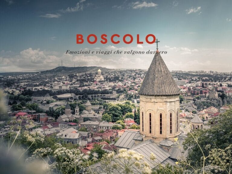 Un paesaggio urbano della Georgia con il campanile di una chiesa in primo piano e colline che ricordano l'Armenia sullo sfondo, sotto un cielo parzialmente nuvoloso.