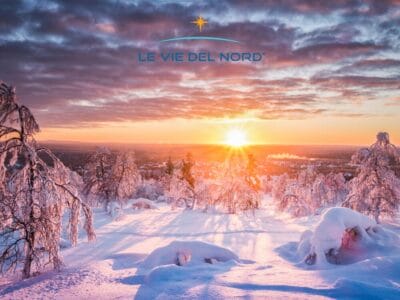 Alberi innevati sotto un cielo colorato dal tramonto catturano la magia della Lapponia Svedese, con il logo "Le Vie Del Nord" in cima, perfetto per la vostra avventura a Capodanno o al Tour Luleå.