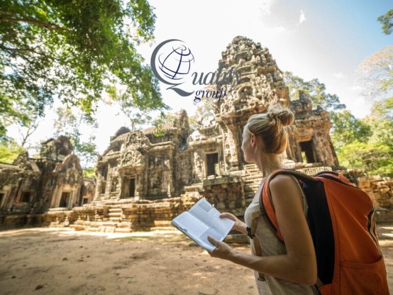 Una donna con uno zaino regge una guida turistica mentre esplora le rovine di antichi templi circondati da alberi durante il suo tour in Cambogia.
