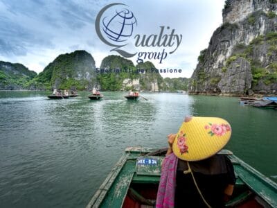 Una persona con un cappello è seduta su una barca in una baia pittoresca, con scogliere rocciose e altre imbarcazioni nelle vicinanze, e si gode un'autentica esperienza del Tour Vietnam.