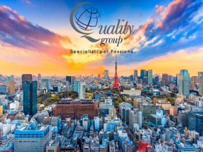 Tramonto colorato sullo skyline di Tokyo con la Tokyo Tower, che cattura lo spirito del Giappone. Il logo e lo slogan "Quality Group" sono sovrapposti in alto.