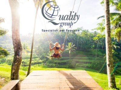 Donna su un'altalena con vista sulle lussureggianti terrazze di riso verdeggianti di Bali, perfetta per il tuo prossimo post su Instagram, con il logo "Quality Group" e il testo in italiano sopra.
