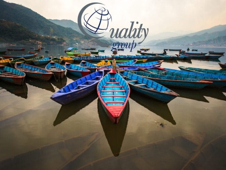 Barche di legno colorate disposte in cerchio su un tranquillo lago nepalese con montagne sullo sfondo, perfette per un tour panoramico. Logo sovrapposto in alto.