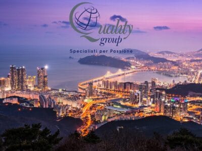 Paesaggio urbano al tramonto con edifici illuminati, un ponte e la scritta "Gruppo qualità" sovrapposta in alto, che cattura lo spirito vibrante di un'avventura del Tour Corea del Sud.