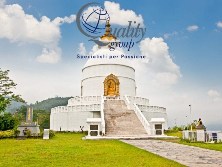 Uno stupa bianco con porte dorate si erge sotto un cielo azzurro in Nepal, con la scritta "Gruppo di qualità" e un globo sopra, a evocare lo spirito del Festival di Dashain.