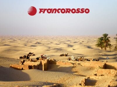 Paesaggio desertico con rovine sparse, cammelli, palme e il logo Francorosso in alto: perfetto per avventure Oasi in 4x4 o indimenticabili tour in Tunisia.