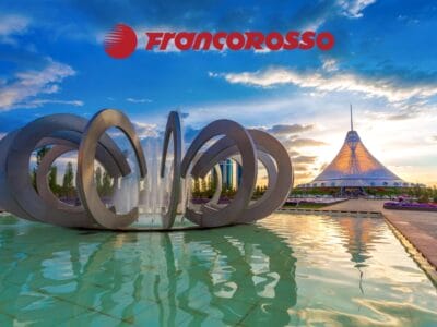 Fontana moderna e tenda Khan Shatyr ad Astana, Kazakistan, al tramonto, dove Tradizioni incontra Modernità, con il logo Francorosso sopra.