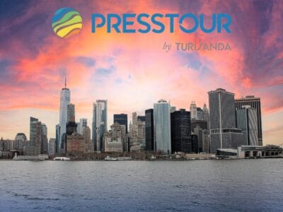 Lo skyline di New York al tramonto con il logo "Presstour by Turisanda" sopra il cielo, che cattura lo spirito vibrante degli Stati Uniti.