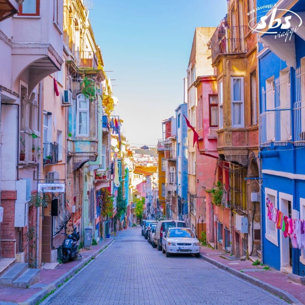 Una strada stretta e colorata, fiancheggiata da auto parcheggiate ed edifici vivaci in un quartiere soleggiato della città.