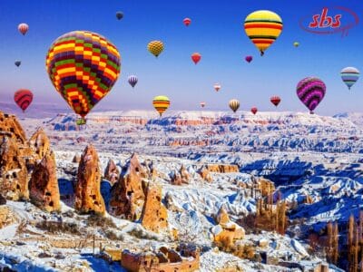Coloratissime mongolfiere fluttuano sul paesaggio roccioso e innevato della Cappadocia sotto un cielo azzurro e limpido: una scena magica in qualsiasi tour della Turchia o in un indimenticabile viaggio invernale.