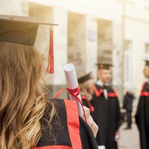 Uno studente con cappello e toga tiene in mano il Diploma IB, di fronte a compagni di classe in abbigliamento simile, fuori da un edificio, per celebrare il loro risultato come prepariamo gli studenti per le novità del futuro.