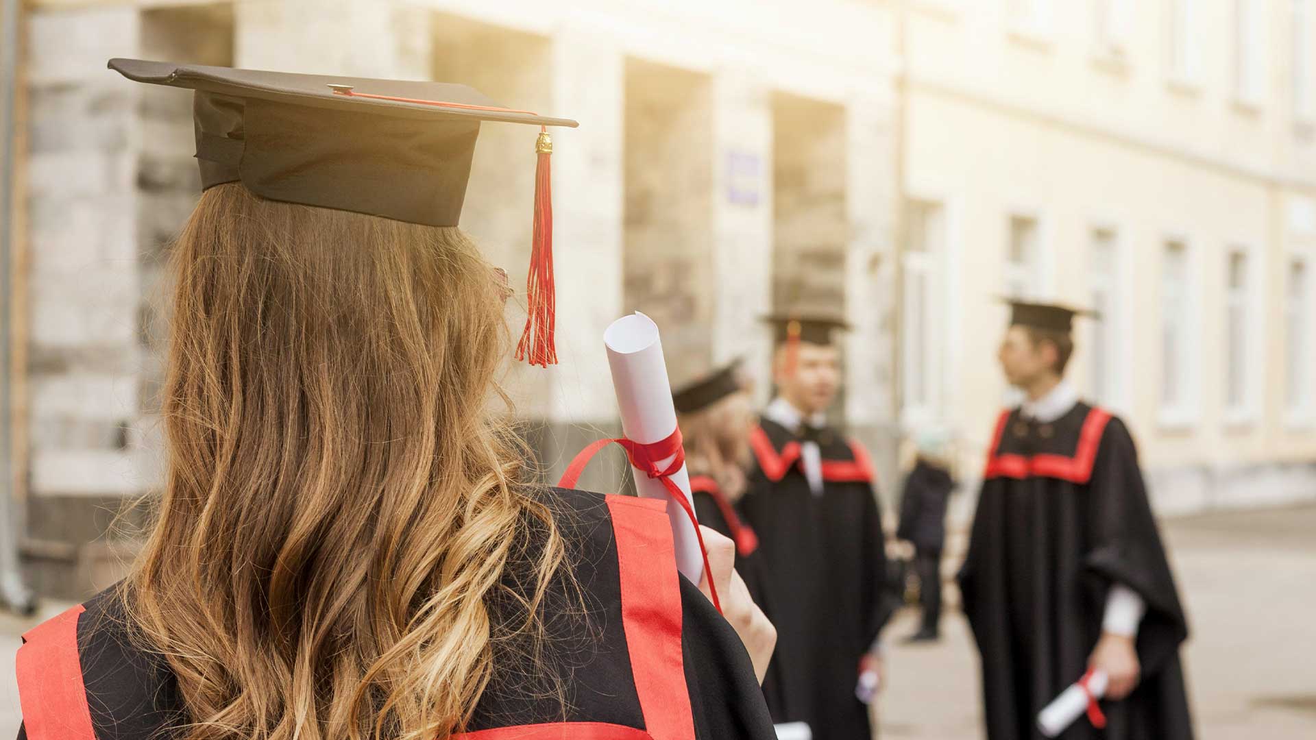 Uno studente con cappello e toga tiene in mano il Diploma IB, di fronte a compagni di classe in abbigliamento simile, fuori da un edificio, per celebrare il loro risultato come prepariamo gli studenti per le novità del futuro.