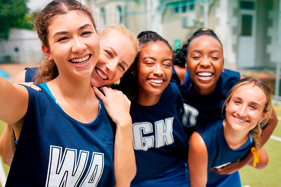 Cinque giovani donne sorridenti che indossano uniformi sportive blu posano insieme all'aperto, apparendo felici ed energiche, probabilmente dopo una partita sportiva di squadra.