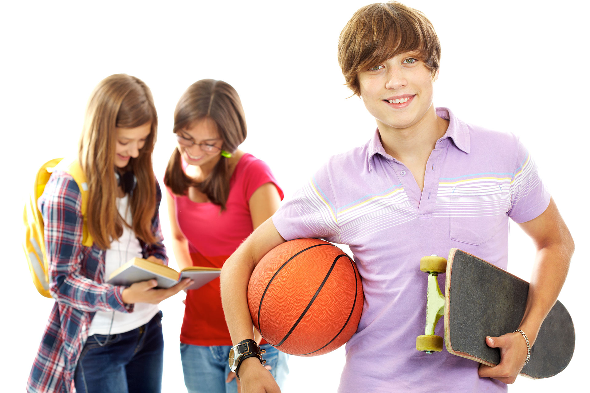 Un ragazzo adolescente con in mano un pallone da basket e uno skateboard sorride alla telecamera, mentre due ragazze sullo sfondo leggono un libro insieme, con un'aria rilassata e disinvolta.