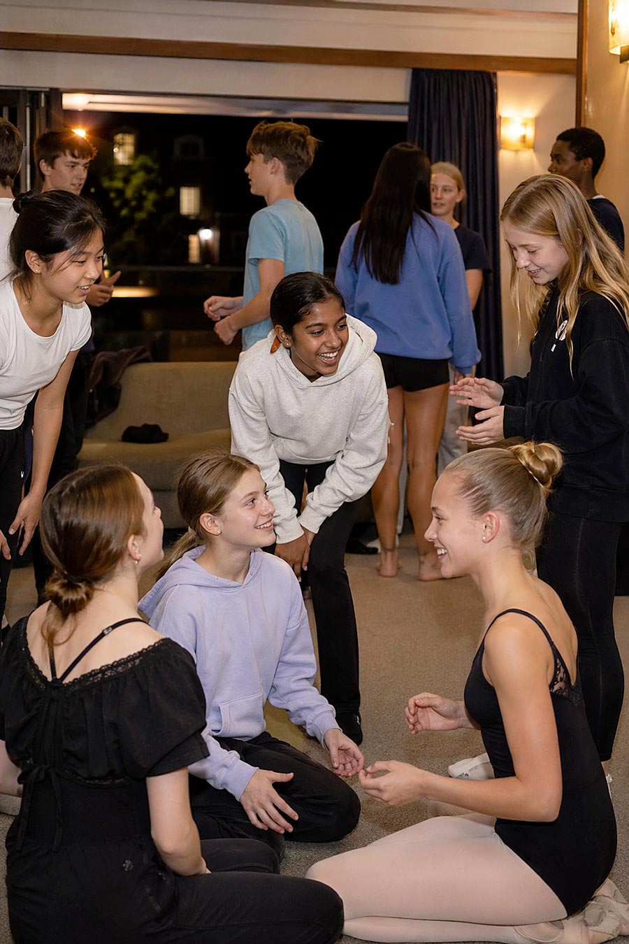 Un gruppo di adolescenti, alcuni in tenuta da Accademia di danza, sorride e chiacchiera al chiuso. Sembrano rilassati e felici, godendosi un incontro sociale informale.