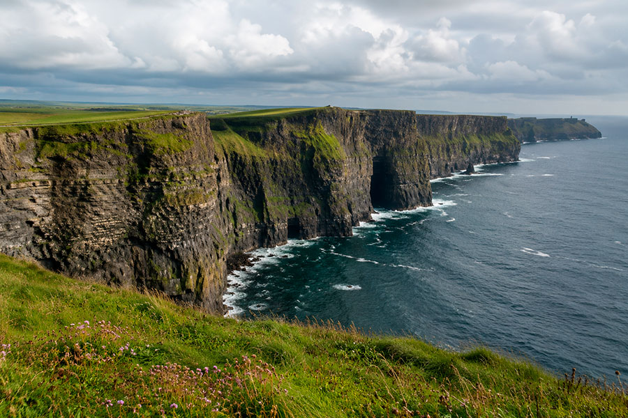 Ripide scogliere verdi si ergono sopra l'Oceano Atlantico, con le onde che si infrangono contro la costa rocciosa sottostante: una vista mozzafiato per gli studenti che si godono il loro quarto anno in Irlanda sotto un cielo nuvoloso.