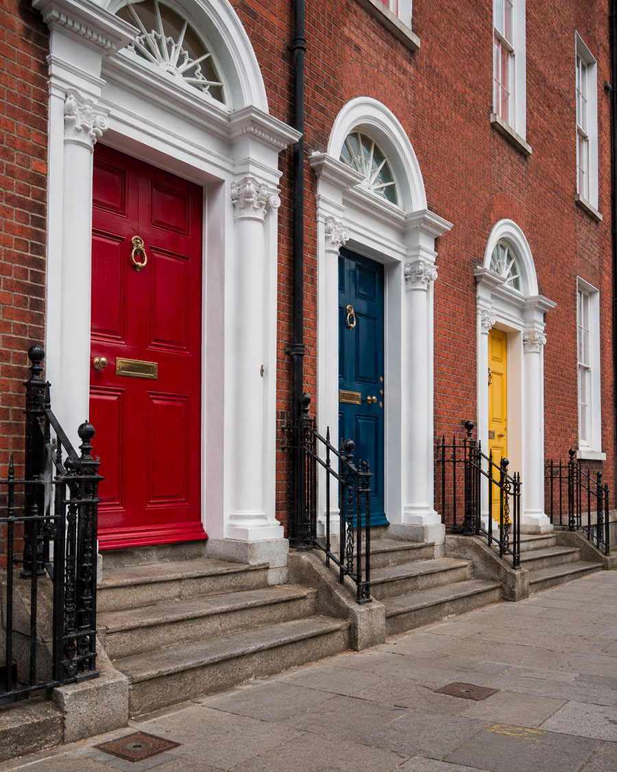 Tre coloratissime porte georgiane - rossa, blu e gialla - incastonate in cornici bianche con sopraluce, fiancheggiano un edificio in mattoni. Provate questo fascino durante la vostra avventura nel quarto anno Irlanda o nell'anno scolastico Irlanda.