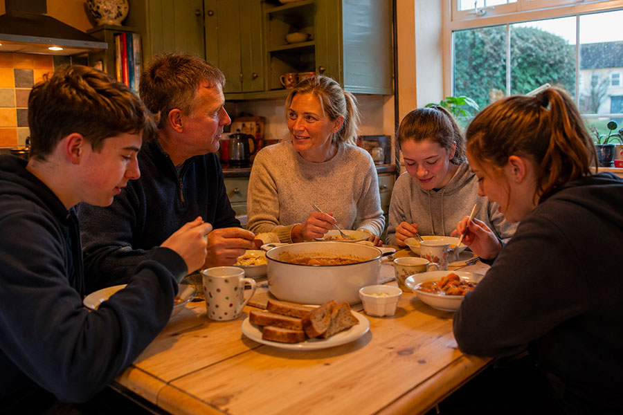 Una famiglia di cinque persone siede intorno a un tavolo da cucina in legno, condividendo un pasto accogliente. La loro calda riunione riecheggia il senso di unione che spesso si prova durante un anno scolastico in Irlanda.
