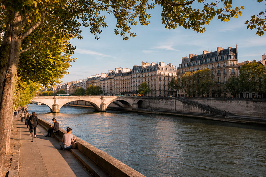 Le persone si rilassano e passeggiano lungo il lungofiume alberato della Senna a Parigi, ammirando i classici edifici di Haussmann: una scena perfetta per chi trascorre un anno scolastico in Francia in una giornata di sole.