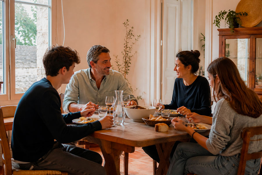 Quattro persone siedono intorno a un tavolo da pranzo in legno, condividendo il pasto e sorridendo l'uno all'altro in una stanza caldamente illuminata: l'ideale per discutere di un anno scolastico in Francia o per pianificare insieme un'esperienza di anno all'estero Francia.